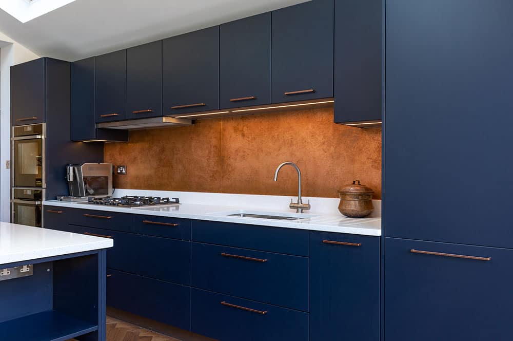 Antique Copper Splashback with Navy Blue Kitchen Cabinets - Designs 05 long aged copper splashback with warm patina in modern blue kitchen.