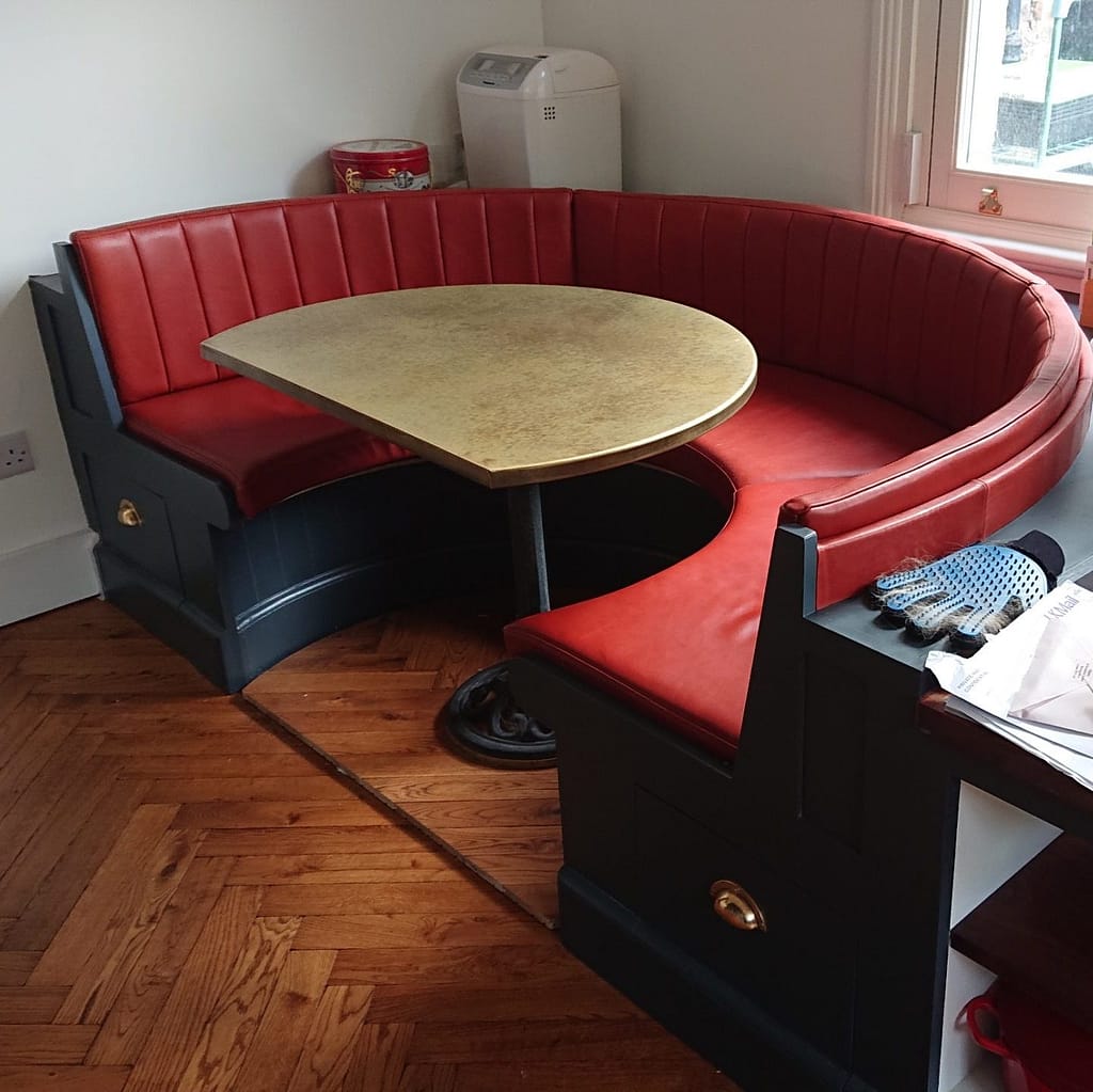 D-Shaped Brass Table – Custom Booth Seating - Designs 05 D-shaped brass table with an aged patina, set in a custom-built curved seating area with red leather upholstery