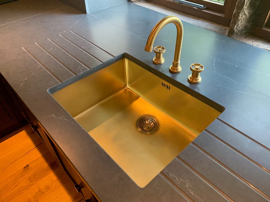 Single Bowl Brass Undermount Sink - Designs 05 A sleek single bowl brass undermount sink, seamlessly installed in a dark stone worktop.