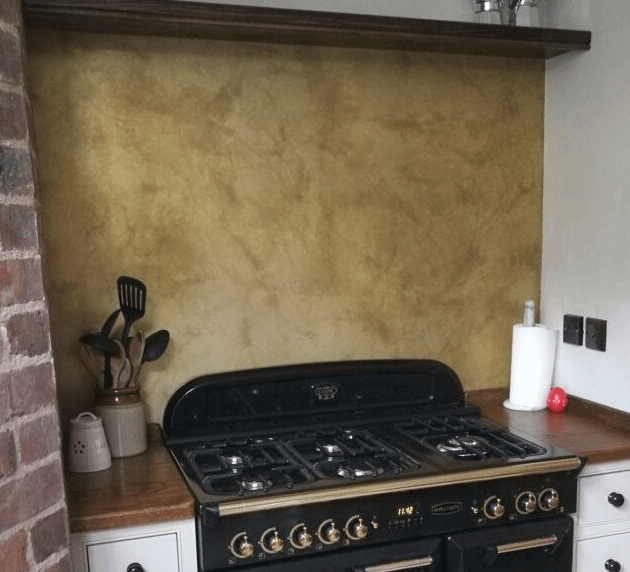 Lightly Aged Brass Splashback - Designs 05 Handcrafted brass kitchen splashback with a soft golden patina, installed behind a traditional gas range, creating a warm and inviting atmosphere.