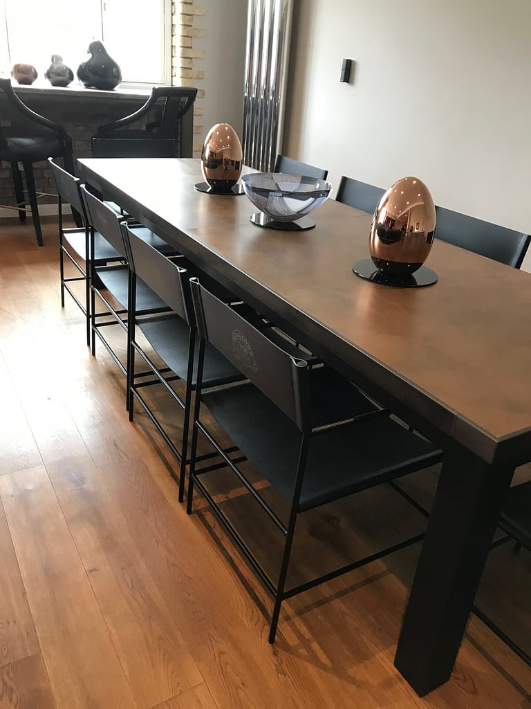Long Copper Dining Table with Black Base and Ornaments Long copper dining table top on a black base frame with copper egg ornaments.