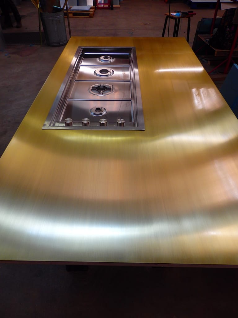 Brass island and hob - Designs 05 Custom brass kitchen worktop with a built-in stainless steel gas hob, featuring a polished brass finish for a sleek, modern aesthetic