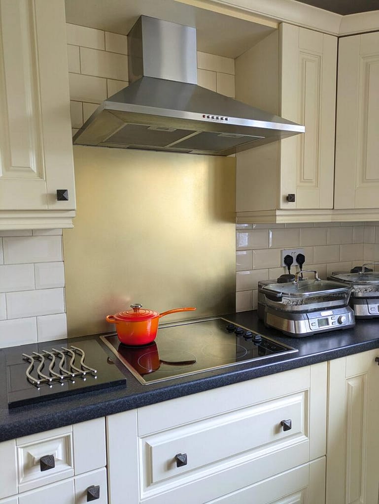 Satin-Brass-Kitchen-Splashback - Designs 05 A second splashback behind a cooker hob, a pan ans steamer in view and yellow cupboards