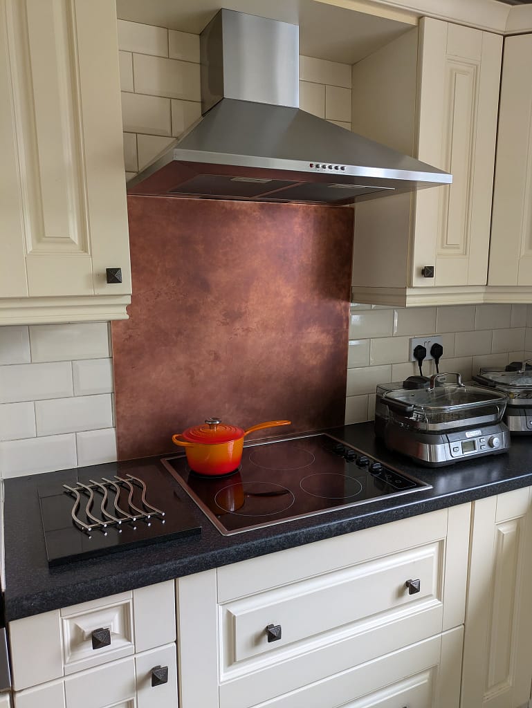 Light Aged Copper Splashback in a Classic Cream Kitchen - Designs 05 Light aged copper kitchen splashback with a soft patina, installed behind a range cooker in a cream shaker-style kitchen.