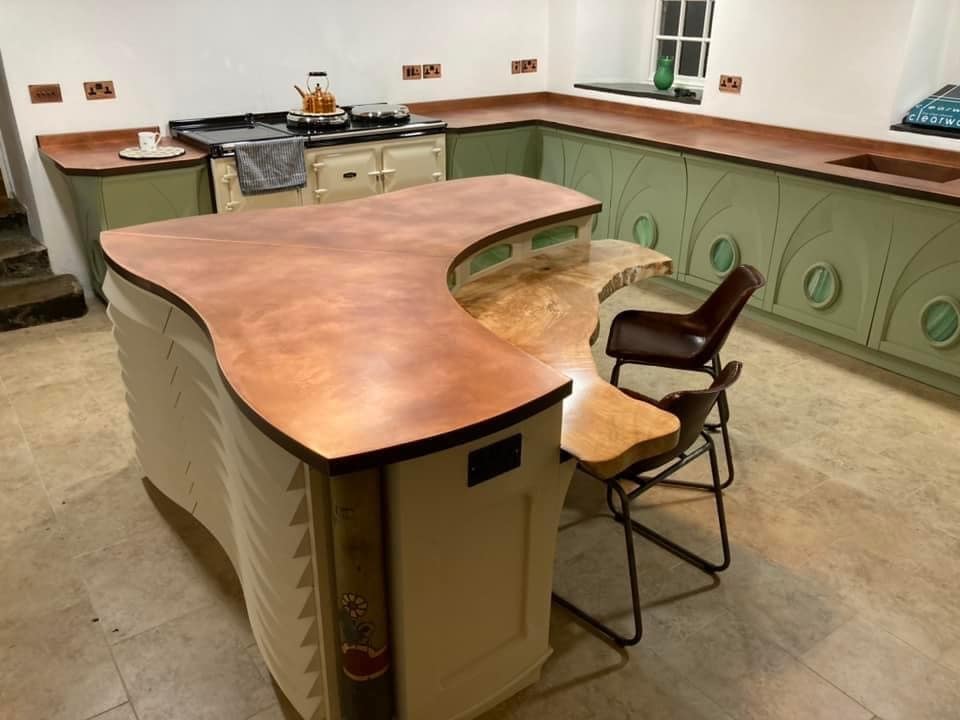 Curved copper kitchen Island worktop - Designs 05 Bespoke curved copper kitchen island worktop with a warm patina finish, paired with a live-edge wooden breakfast bar and sage green cabinetry, creating a rustic yet elegant kitchen design.